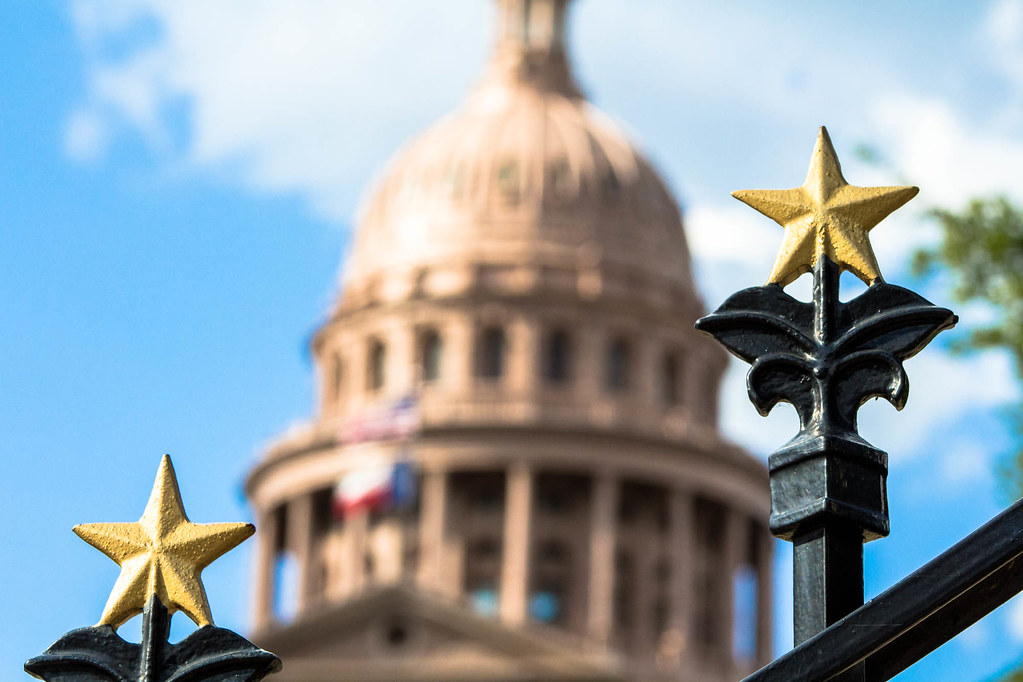 Ornamental stars top a fence in the foreground with the Texas State Capitol dome unfocused in the distant background