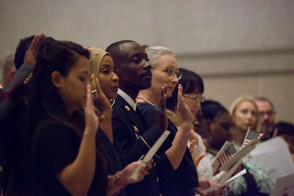 A diverse row of citizenship candidates hold up their right hands as they take the citizenship oath