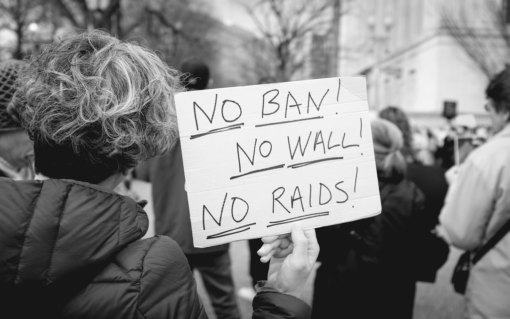 Protester in a crowd holds a sign reading "No Ban! No Wall! No Raids!"