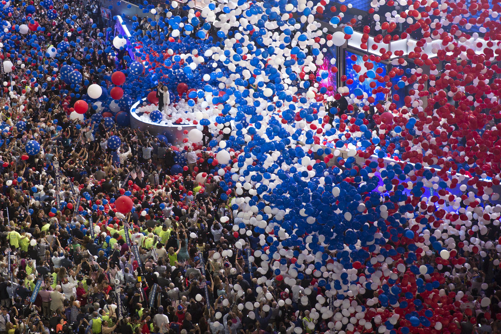 Red, white and blue balloons fall over the crowd on the floor of a large convention