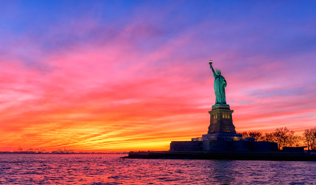 The Statue of Liberty silhouetted against a colorful sunset