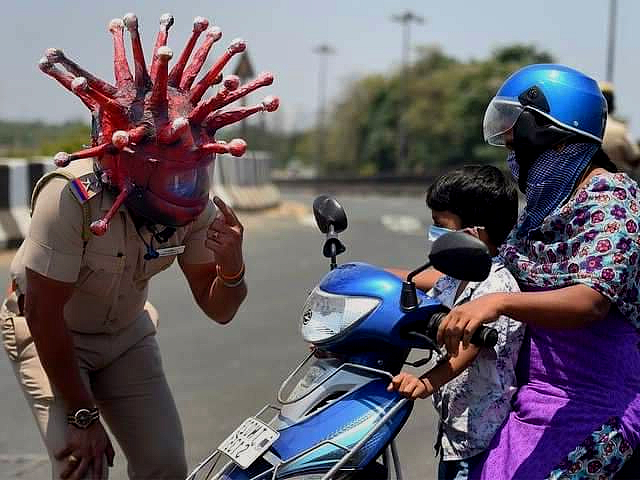 A policeman in a helmet designed to look like a coronavirus cell points to his helmet while speaking to a mother and son an a scooter, encouraging them to return home.