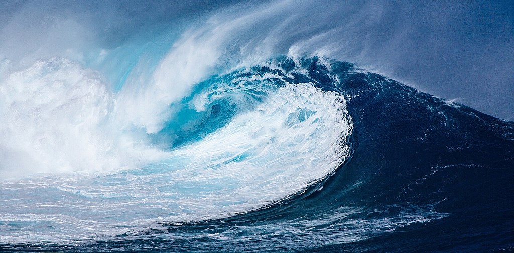 A giant blue ocean wave crashes onto the shore