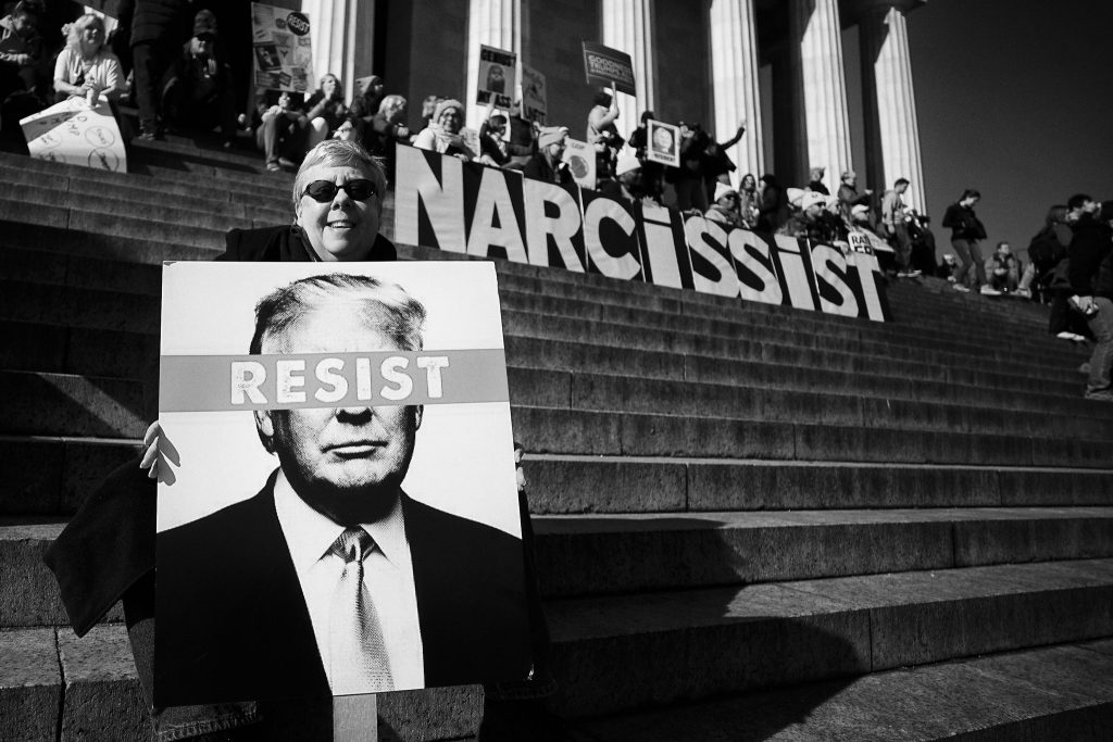 Protest on Capital hill. Signs spell out the word "Narcissit" and "Resist"