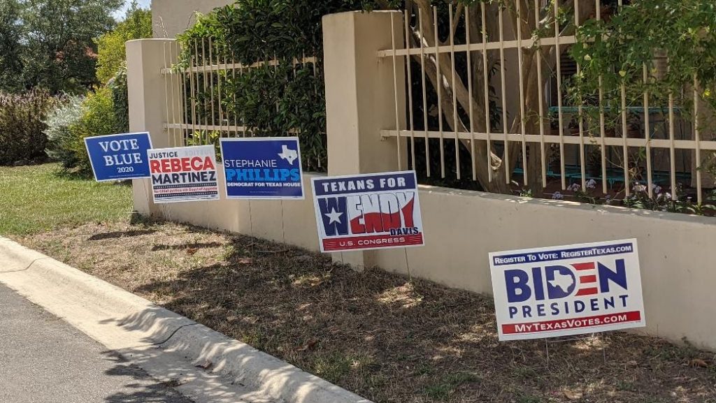 A row of campaign signs in a yard: Biden for President, Texans for Wendy Davis, Stephanie Phillips for HD73, Rebeca Martinez for Judge, Vote Blue 2020