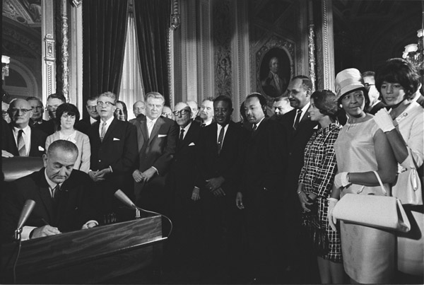 President Lyndon Johnson signs the Voting Rights Act as Martin Luther King, Jr., and other civil rights leaders look on