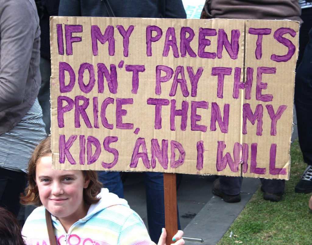 Young girl holding a poster that says "If my parents don't pay the price, then my kids and I will"