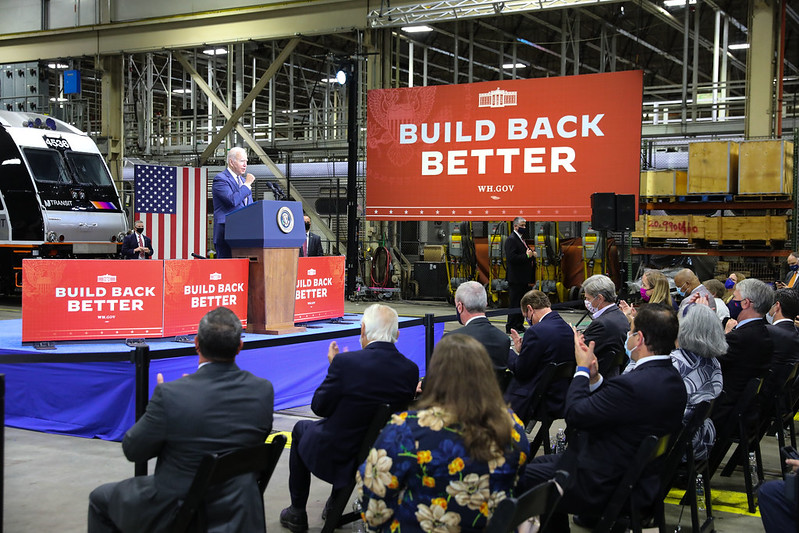 President Joe Biden giving a speech in front of a giant "Build Back Better" sign