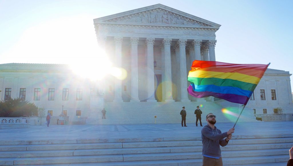Man waving a pride flag in front of the capital of the United States