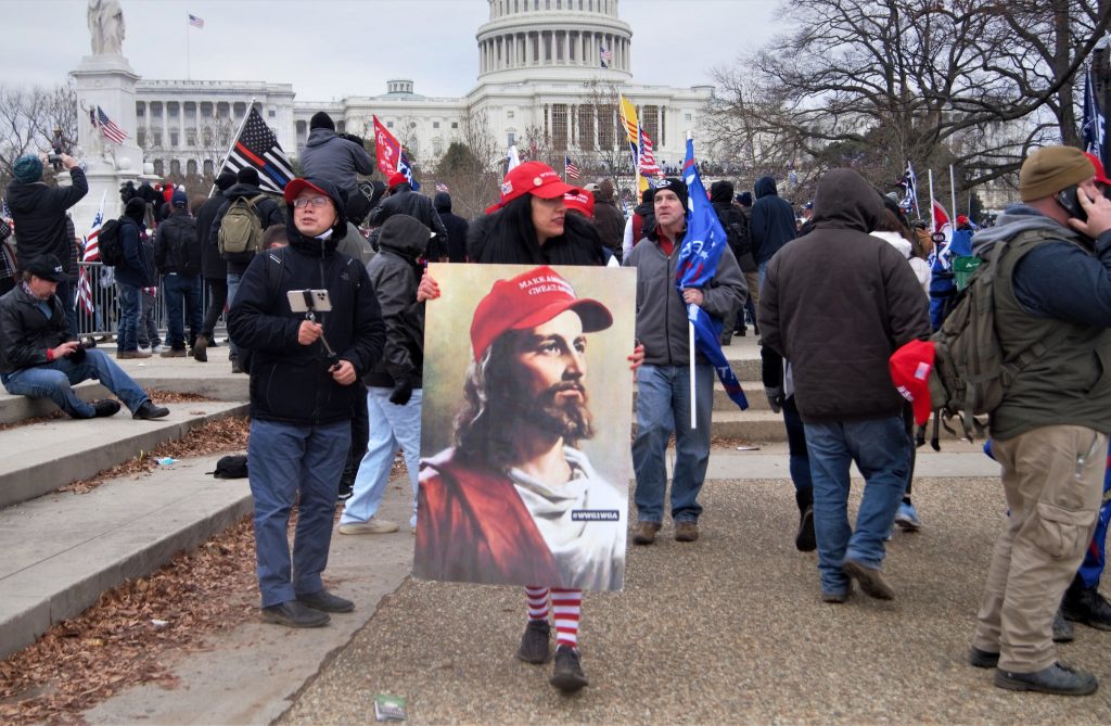 At the January 6 insurrection, a woman holding a picture of Jesus wearing a MAGA hat.