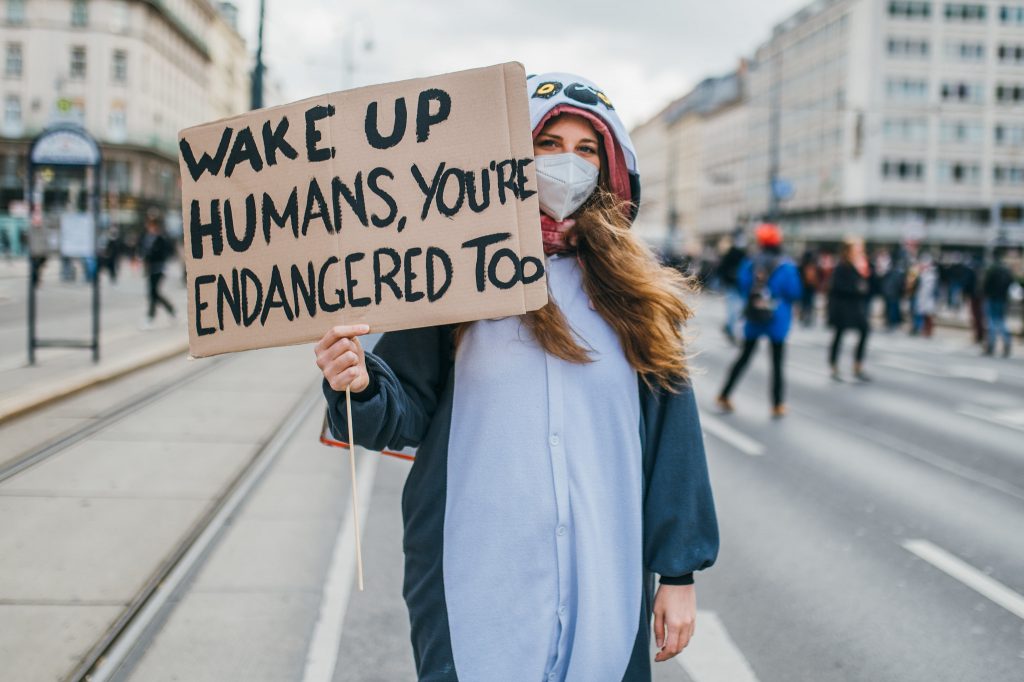 Woman holding a sign which reads "Wake Up Humans, You're Endangered Too"