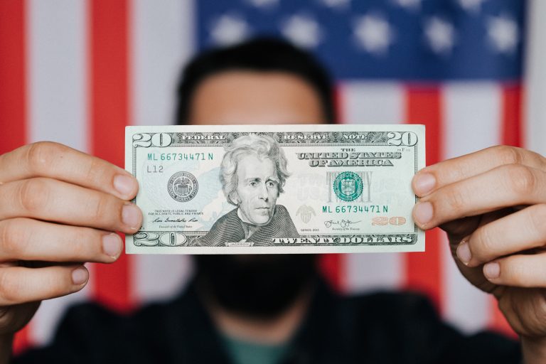 Man holding twenty dollar bill; American flag in background