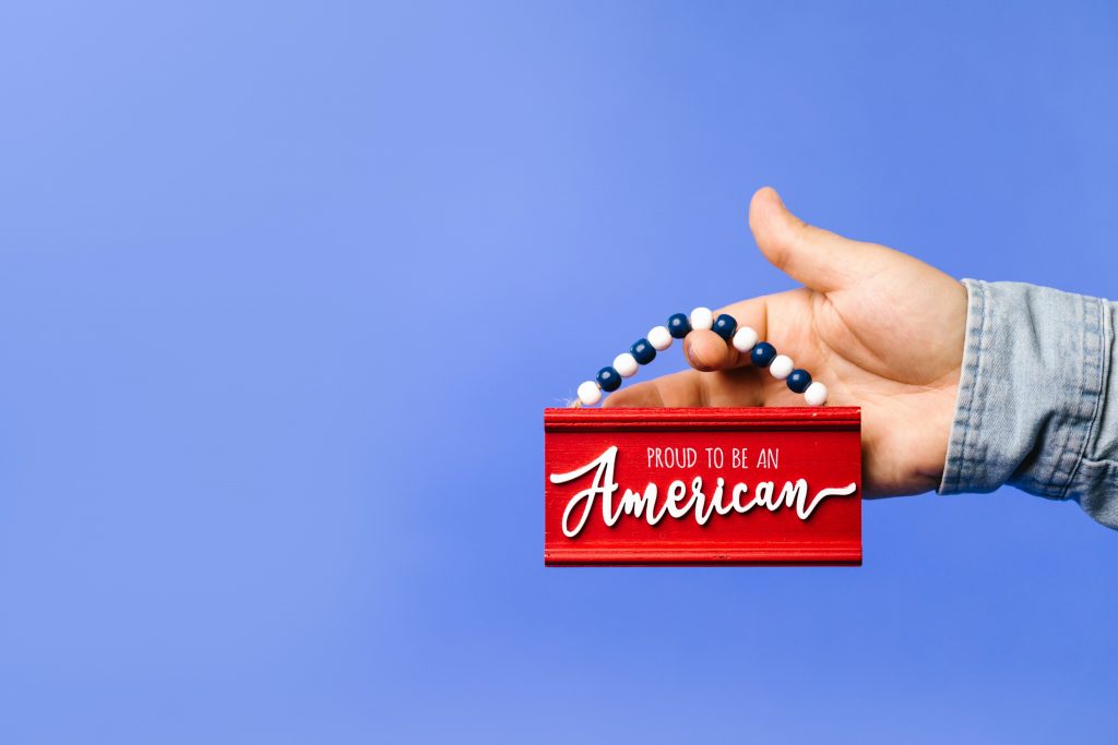 Hand holding sign with "Proud to be an American".