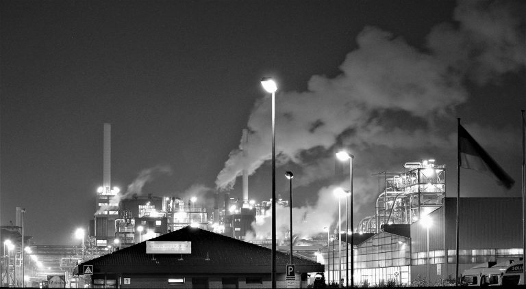 Grayscale photograph of factory with towers spouting emissions.