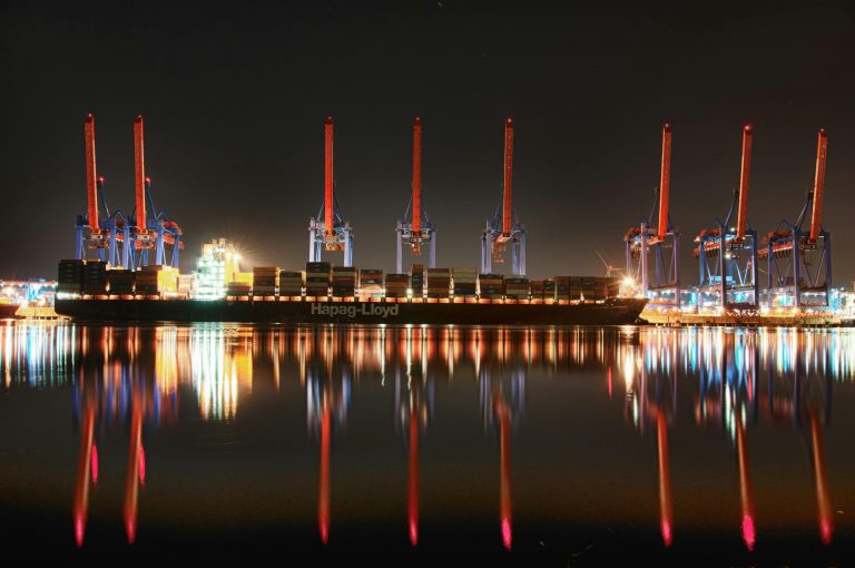 8 large cranes at night with cargo ship in foreground