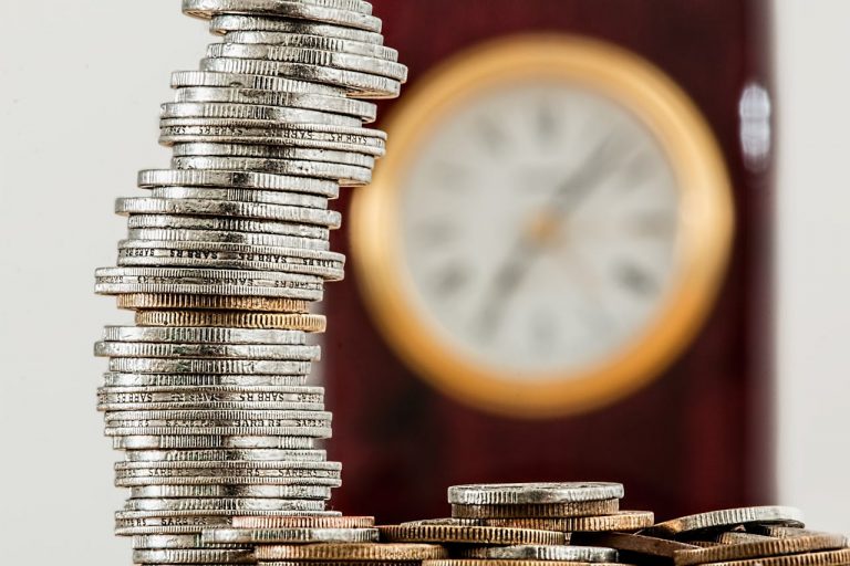 Stacked coins with blurred circular clock in background.